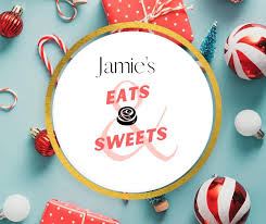 A round white sign with a gold border reading 'Jamie's Eats & Sweets' in black and pink lettering, surrounded by red and white holiday ornaments, candy canes, and wrapped gifts on a light blue background.
